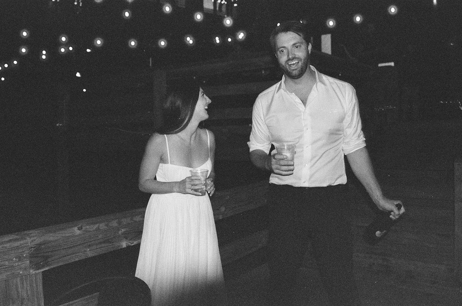 Bride and groom walking with drinks at night during laid-back documentary wedding party in Michigan on film.