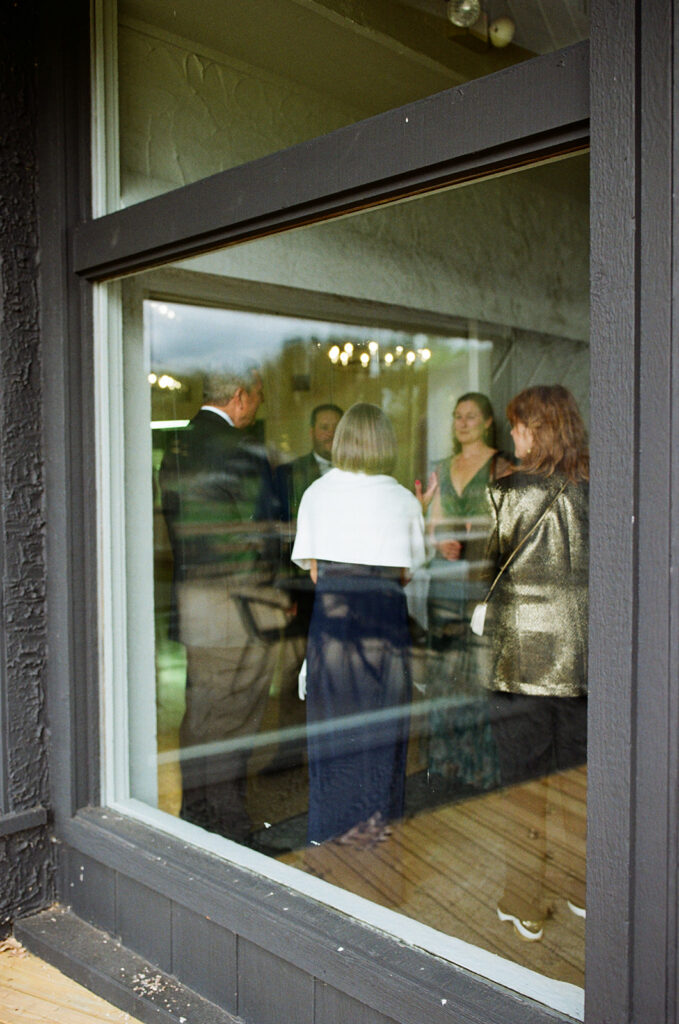 Wedding guests chatting indoors near window during candid Michigan documentary wedding moment on film.