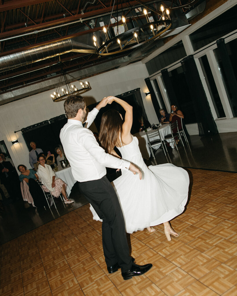 Bride and groom twirling during first dance at indoor wedding reception.