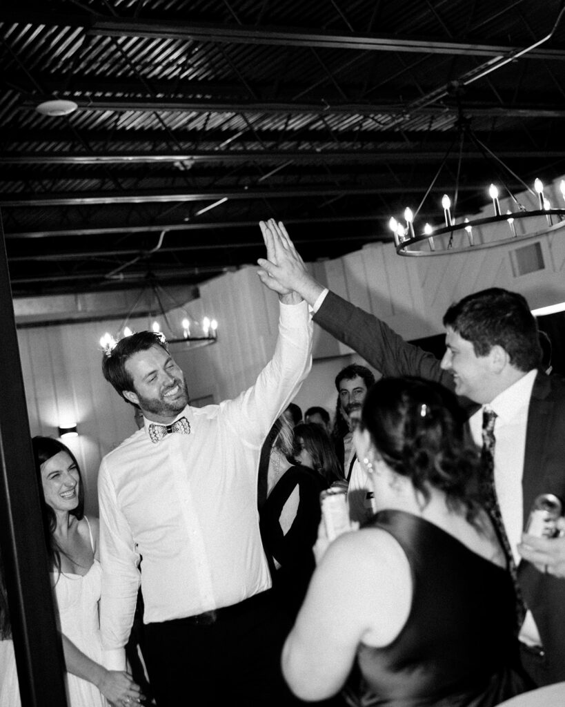 Groom high-fiving guests on crowded dance floor during lively wedding party.