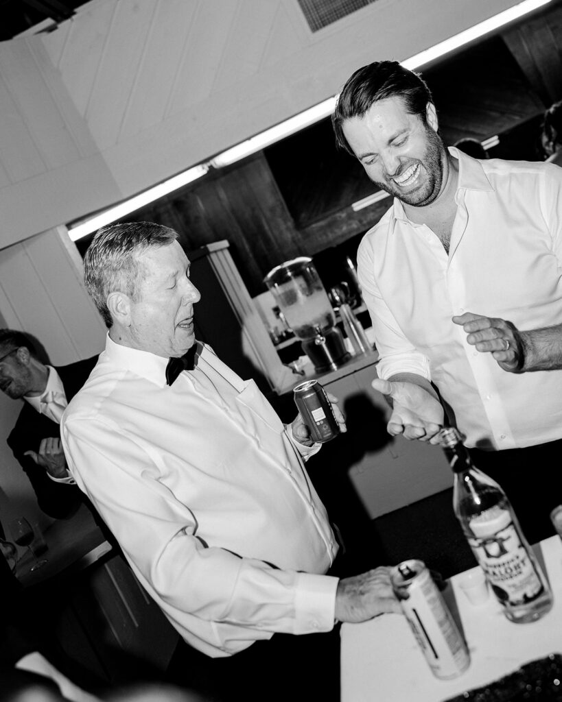 Black and white candid photo of the groom laughing with guests during his Michigan documentary wedding reception.
