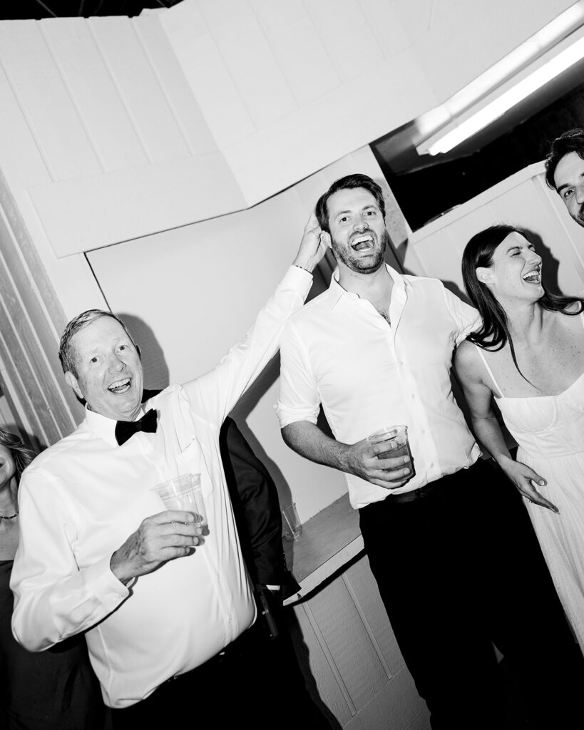 Black and white photo of a bride and groom laughing with guests.