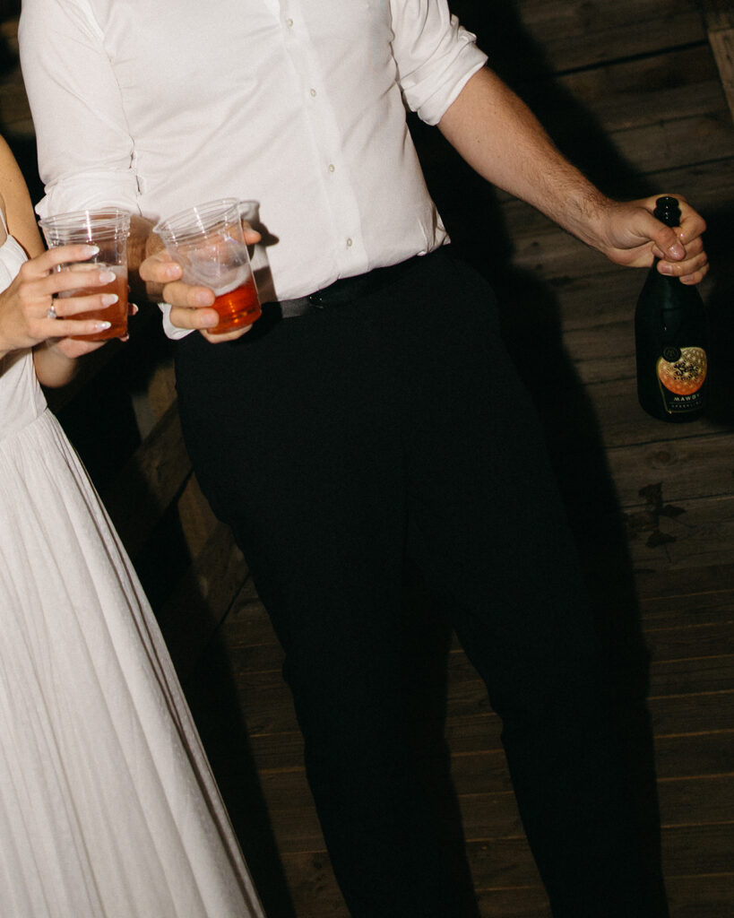 Close up photo of a bride and groom holding drinks during their reception. 