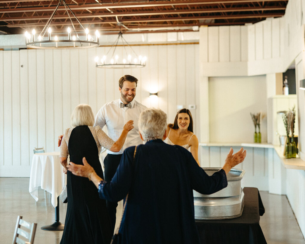 Bride and groom smiling as they greet guests with hugs inside the reception space.