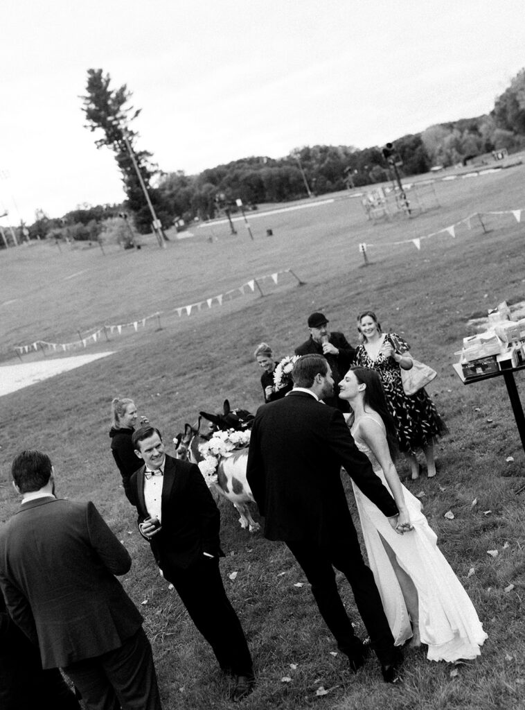Black and white documentary style photo of a bride and groom sharing a private moment as they're outdoors with guests. 