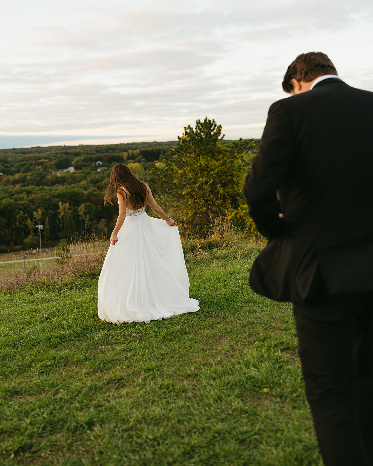 Bride walking through grassy hill at sunset during documentary wedding in Michigan.
