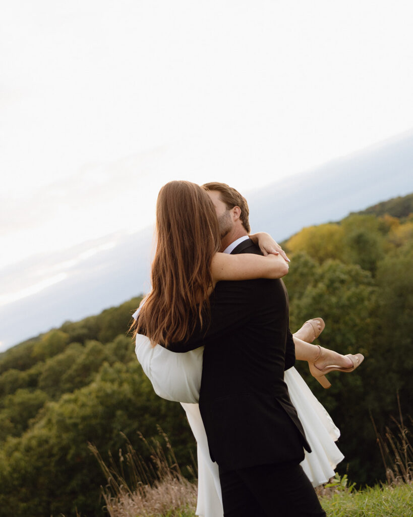Documentary Michigan wedding photo of a groom kissing and lifting his bride during their outdoor portraits.