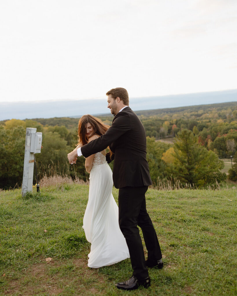 Groom and bride dancing while overlooking scenic Michigan landscape during sunset.
