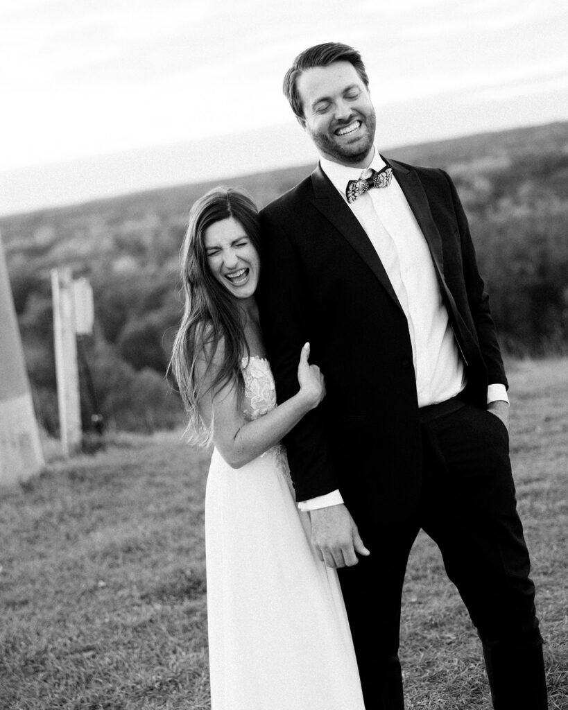 Black and white candid wedding photo of couple laughing together outdoors.
