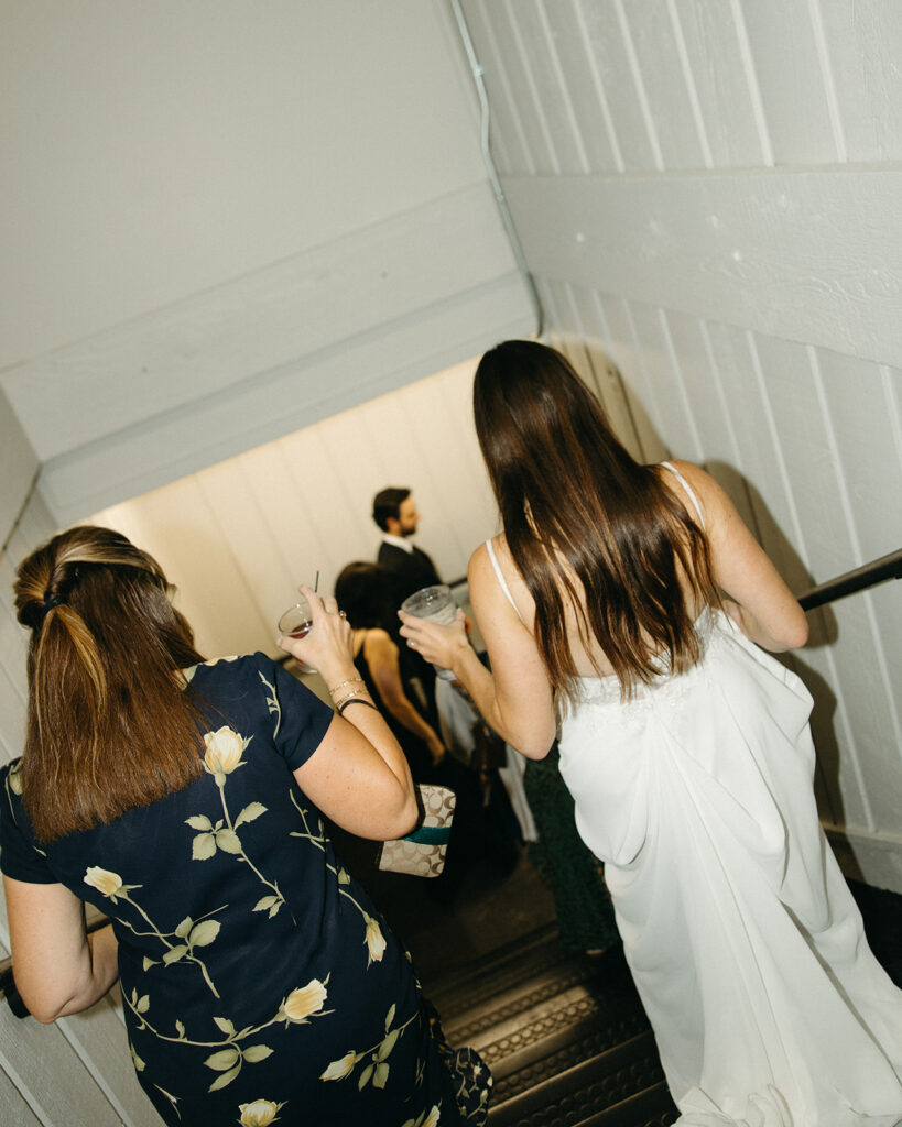 Documentary style wedding photo of a bride walking with guests downstairs. 