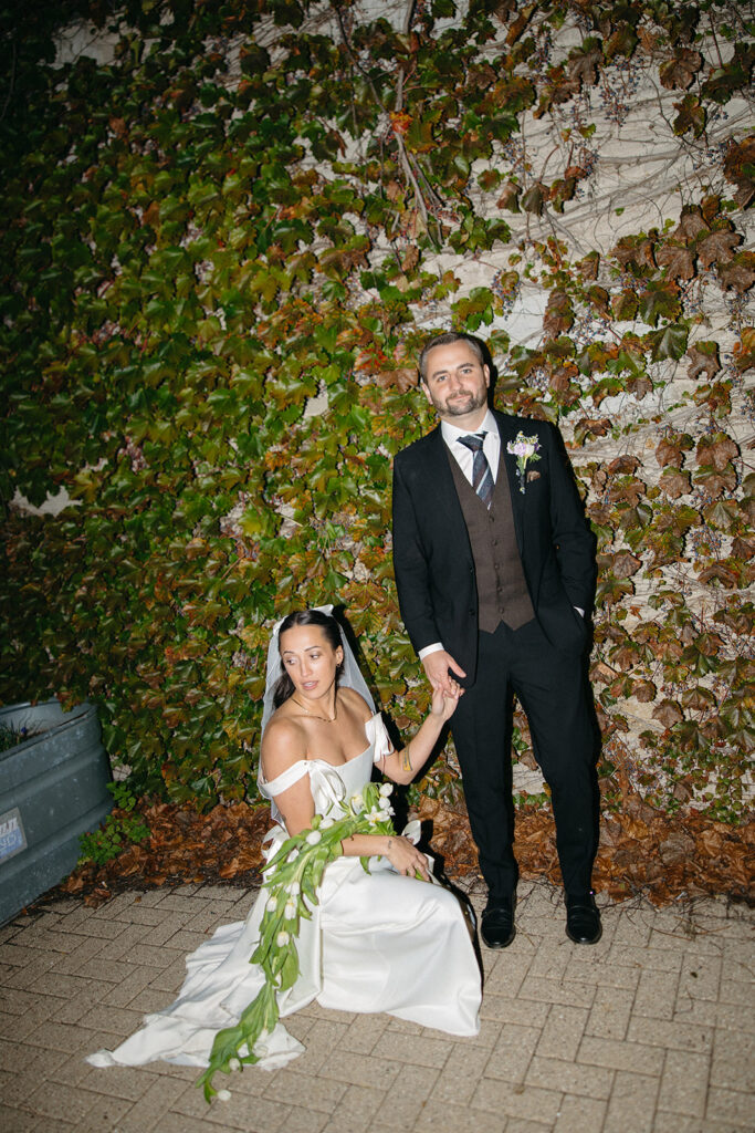 Flash night portrait of a bride and groom posing in front of an ivy-covered wall.