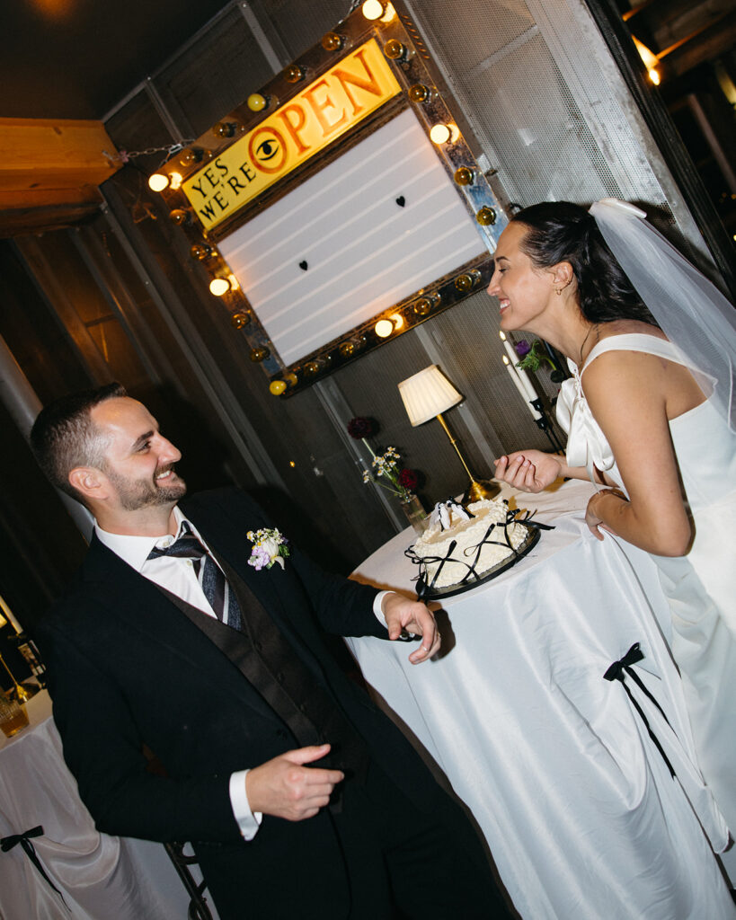 Bride and groom tasting their wedding cake with penguin toppers at Clarkston Michigan wedding reception.