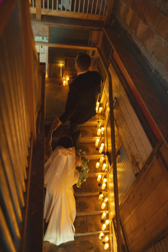 Bride and groom walking up candlelit stairs at Unionwood Shop during their Clarkston, Michigan wedding reception.