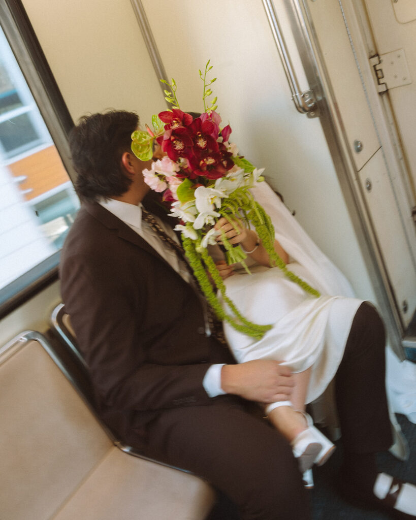Couple kissing behind the brides bouquet as they ride the Detroit People Mover.