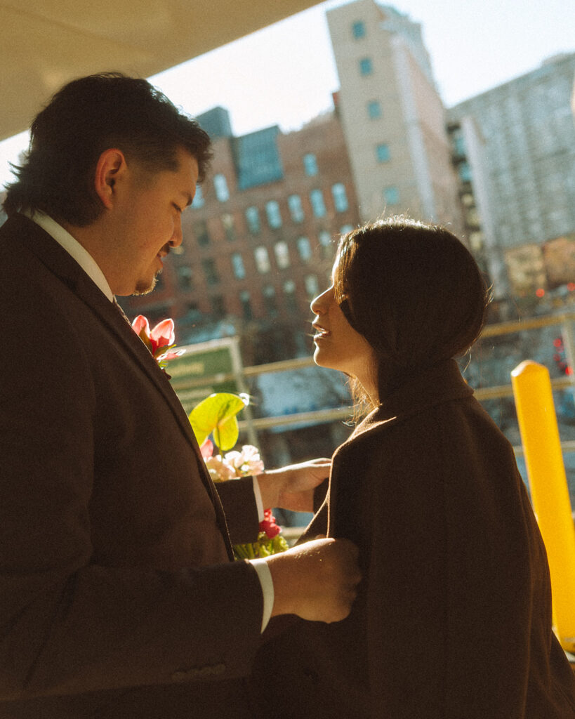 Bride and groom wrapped in coats with golden light at People Mover platform during downtown Detroit elopement.