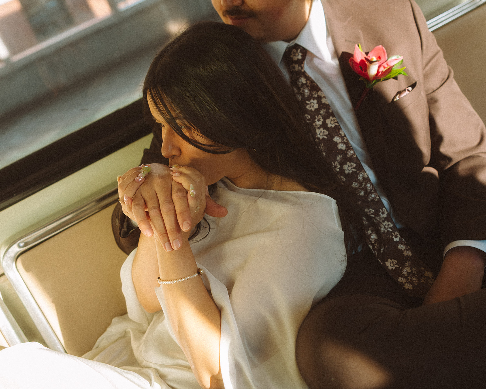 Wide shot of a bride and groom sitting together on the Detroit People Mover as the bride kisses her grooms hand.
