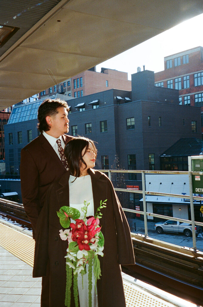 Bride and groom standing on Detroit People Mover platform during downtown Detroit elopement film photo with sunlight.