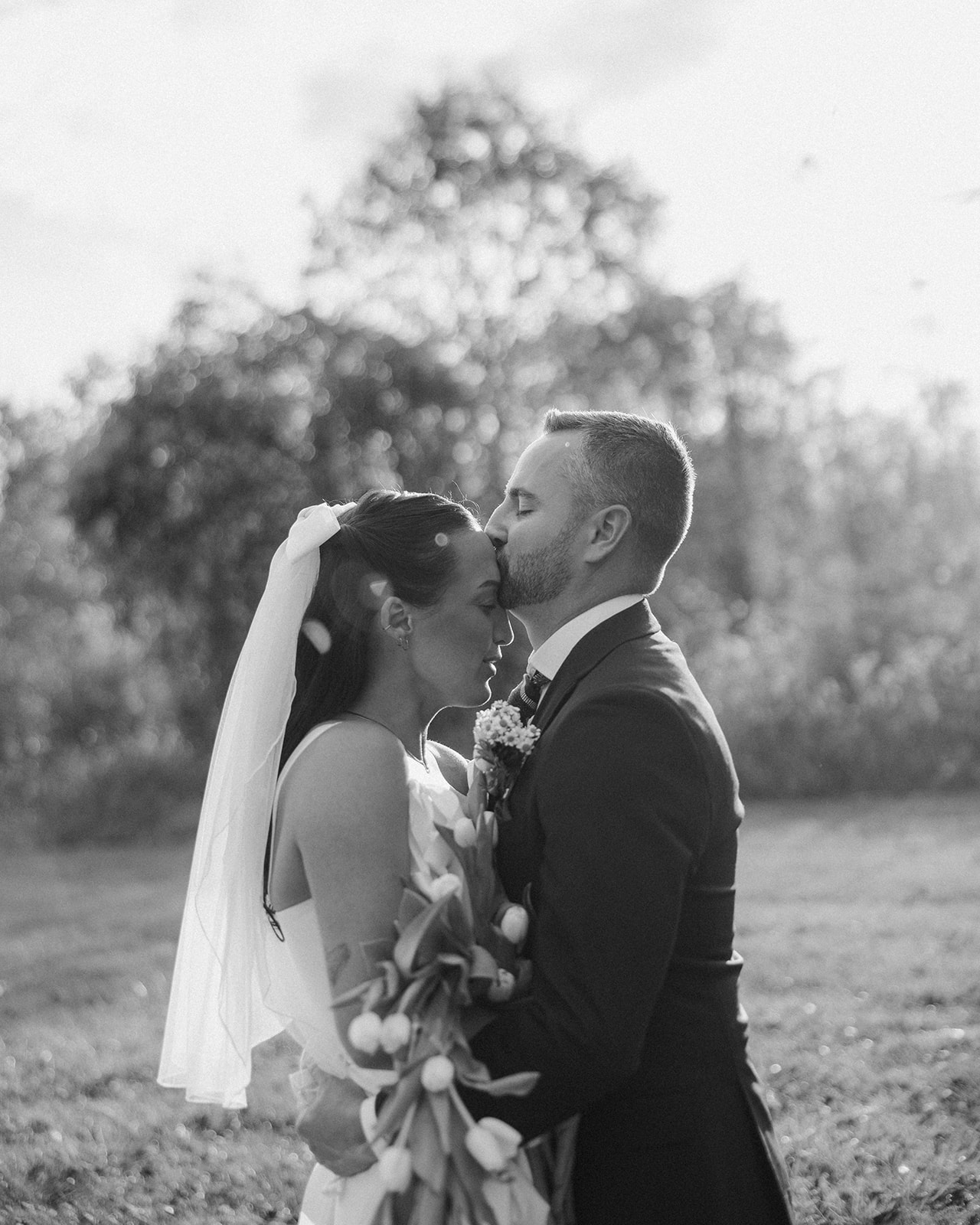 Black and white photo of a groom kissing his brides forehead after their first look.