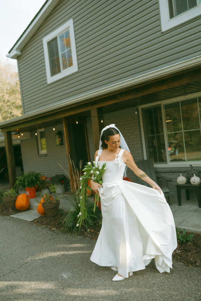 Bride holding her dress outside of her home.
