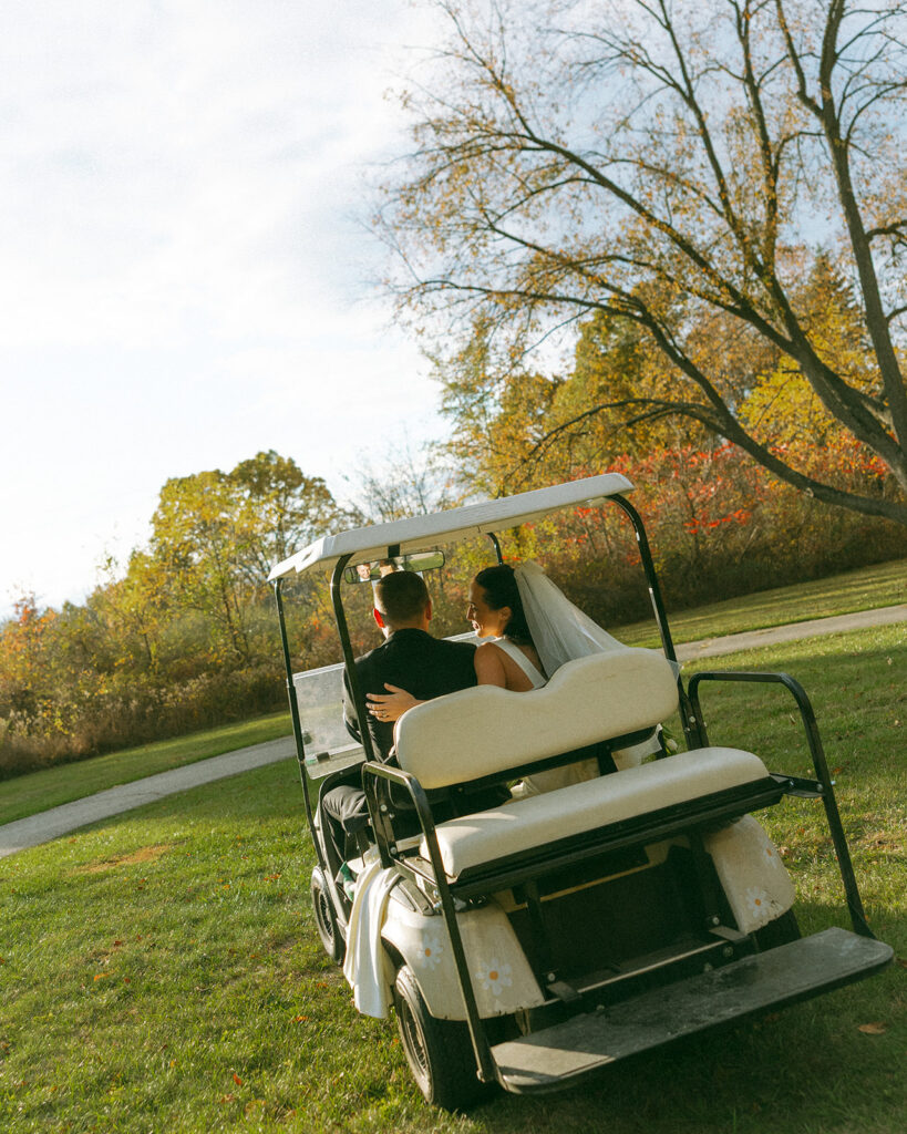 Bride and groom riding in a gold cart on their property.