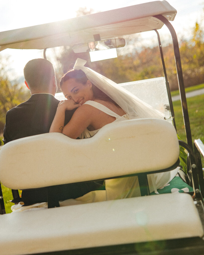 Bride looking back at the camera as her and the groom drive off in a golf cart.