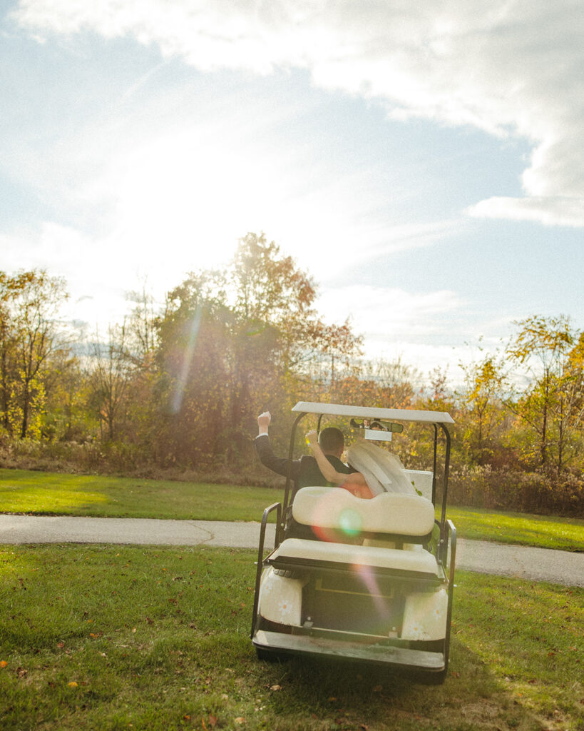 Bride and groom riding off during golden hour in a golf car.