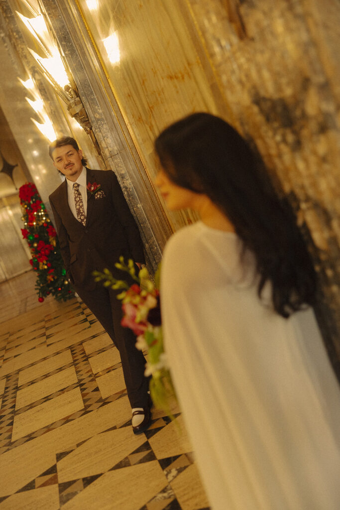 Bride holding bouquet while the groom looks towards her during Fisher Building elopement in Detroit.