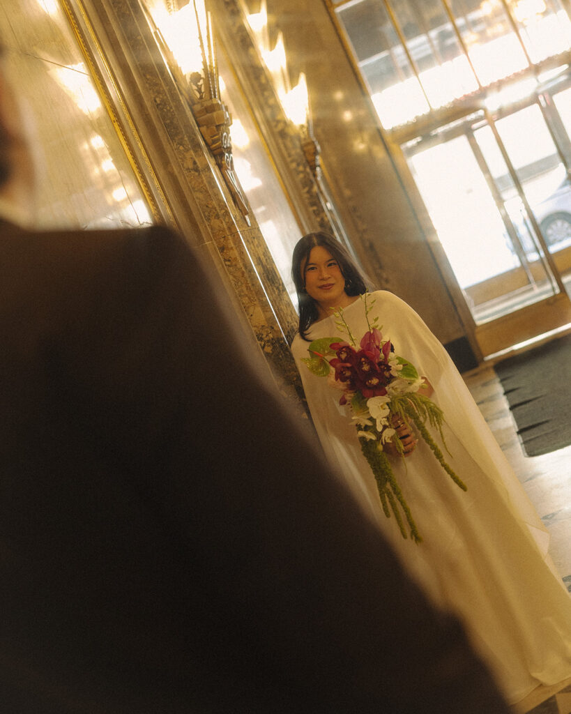 Bride holding bouquet looking toward groom during Fisher Building elopement in Detroit.