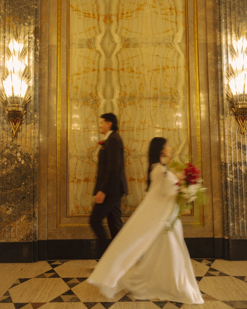 Bride and groom walking past each other in motion blur during fisher building elopement inside art deco interior.