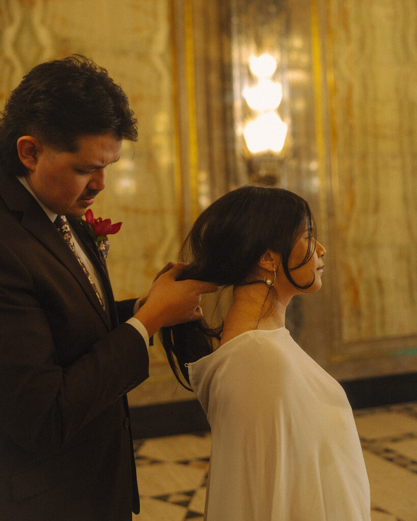 Bride and groom during a fisher building elopement adjusting hair in warm marble interior.