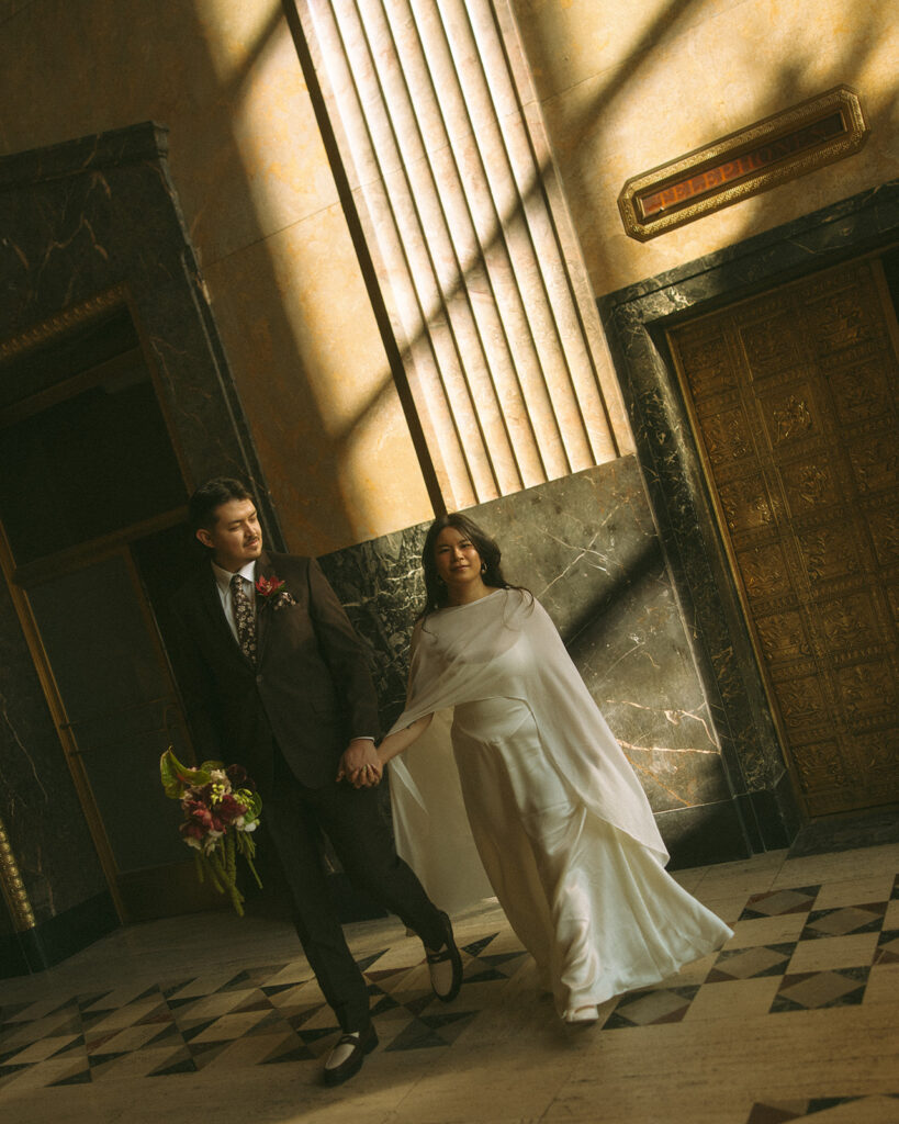 Bride and groom walking hand in hand during Fisher Building elopement with dramatic shadows and architecture.