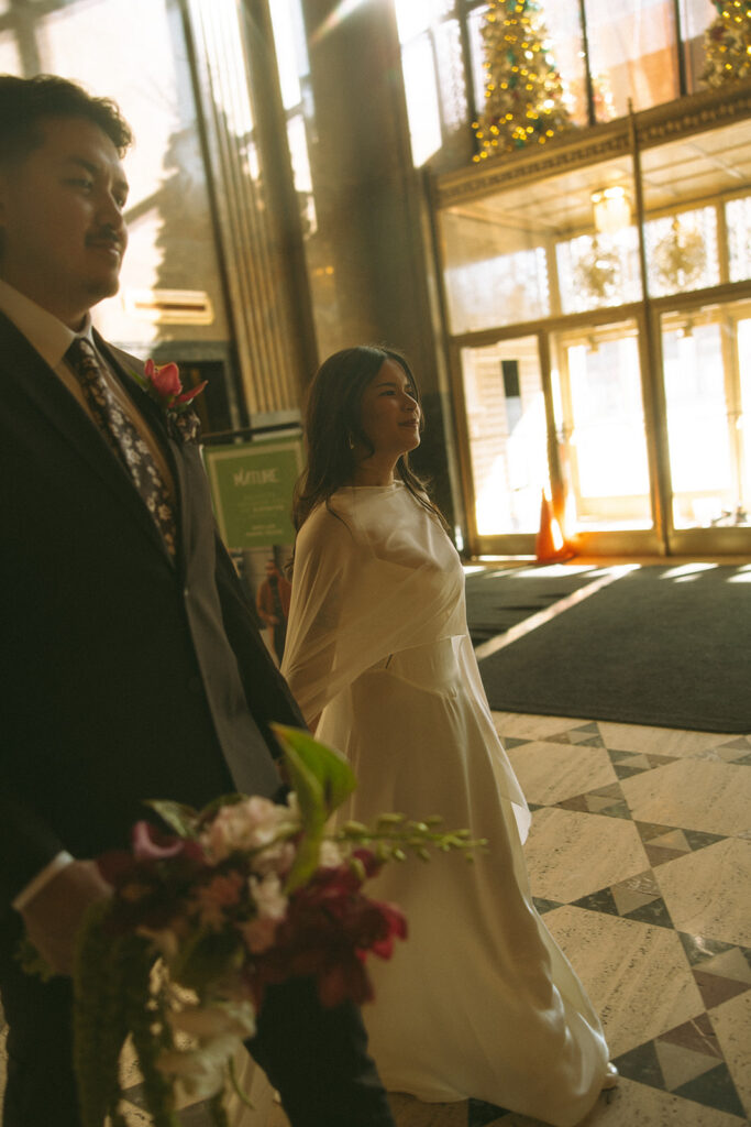 Bride and groom walking hand in hand during Fisher Building elopement with dramatic shadows and architecture.