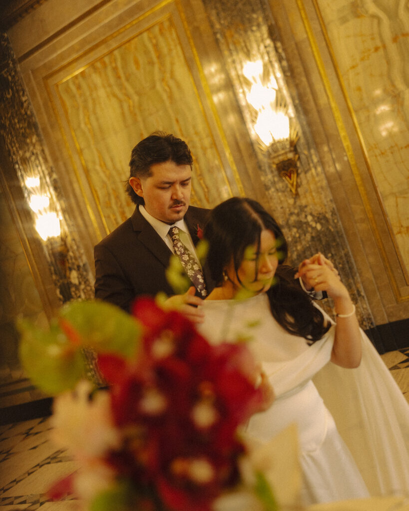 Bride and groom during a fisher building elopement adjusting hair in warm marble interior.