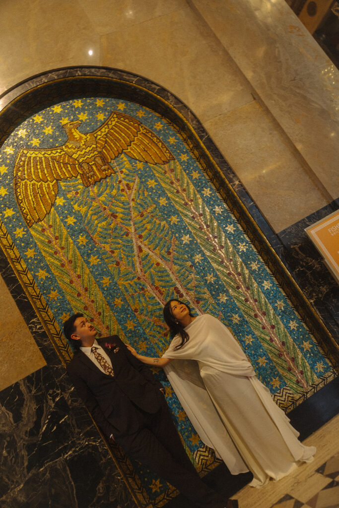 Bride and groom posing under mosaic wall during Fisher Building elopement with colorful art deco details.