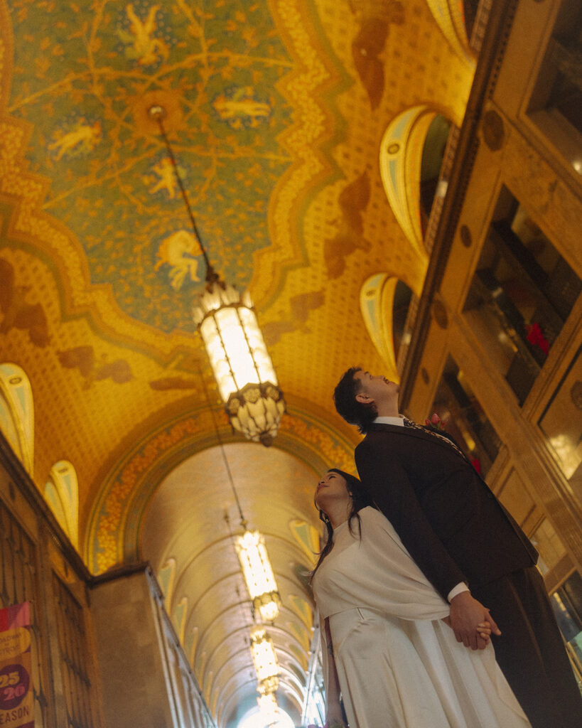 Bride and groom looking up at an ornate ceiling during their Fisher Building elopement with cinematic perspective.
