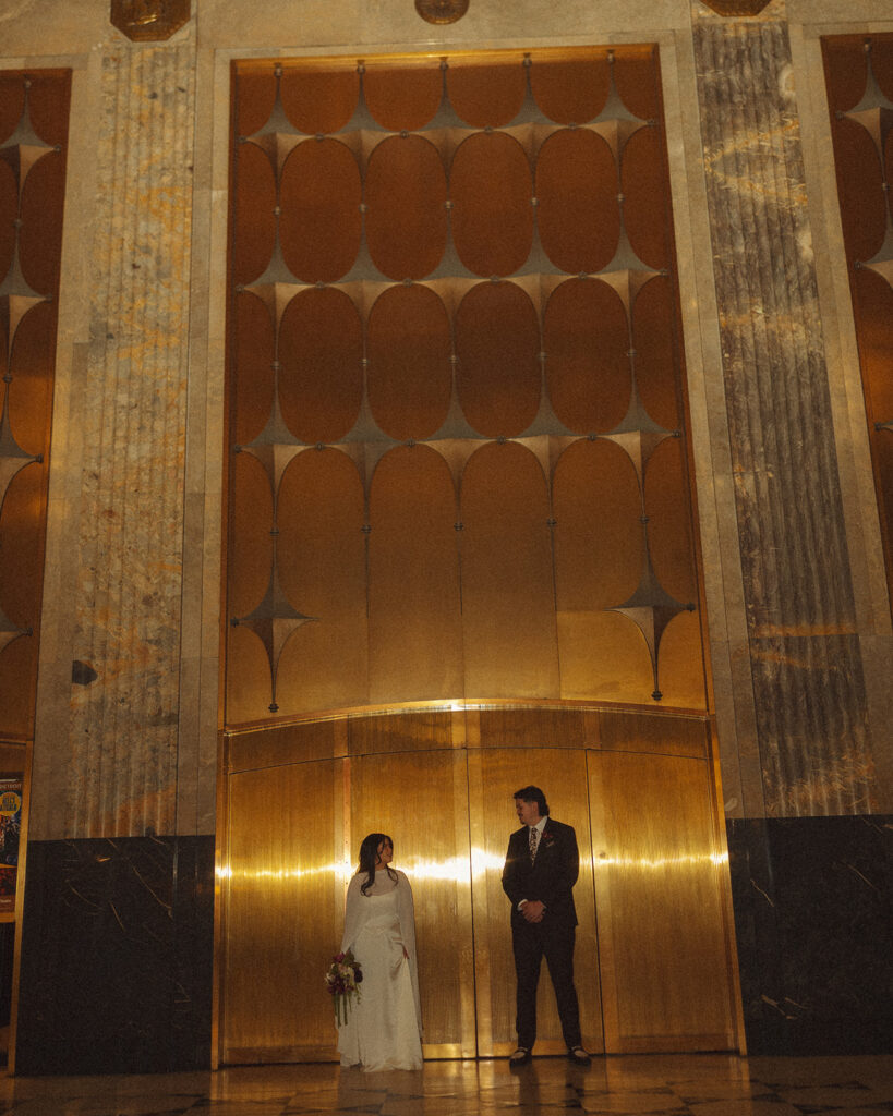 Bride and groom posing in front of a golden wall in Detroit. 