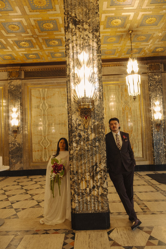 Bride and groom leaning against a column at Fisher Building in Detroit, Michigan.