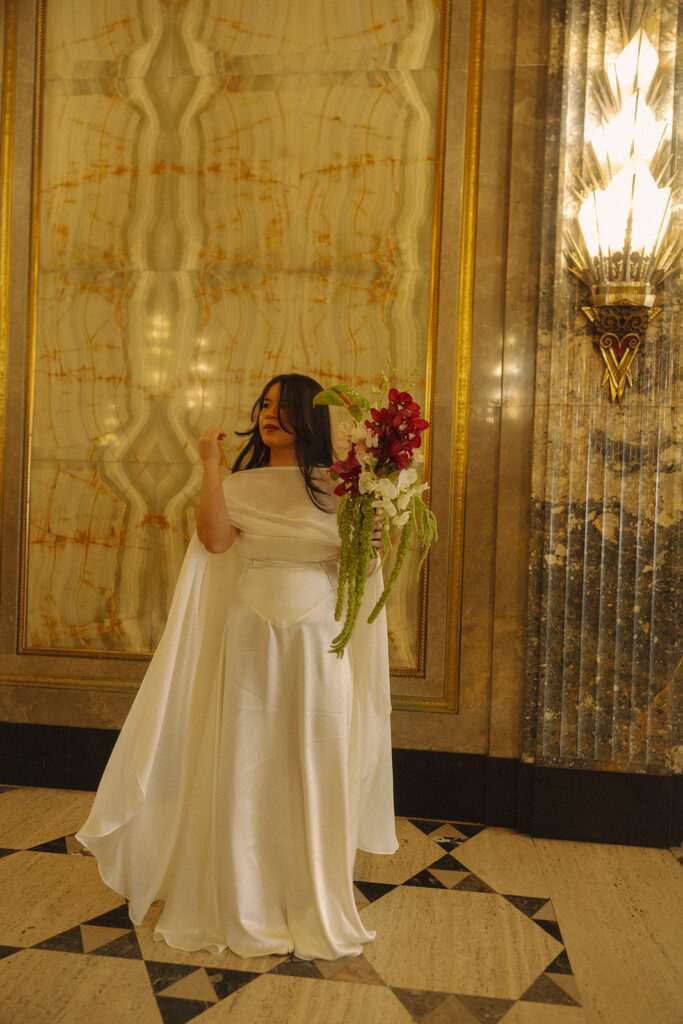 Bride holding bouquet in flowing dress during Fisher Building elopement with art deco wall and soft lighting.