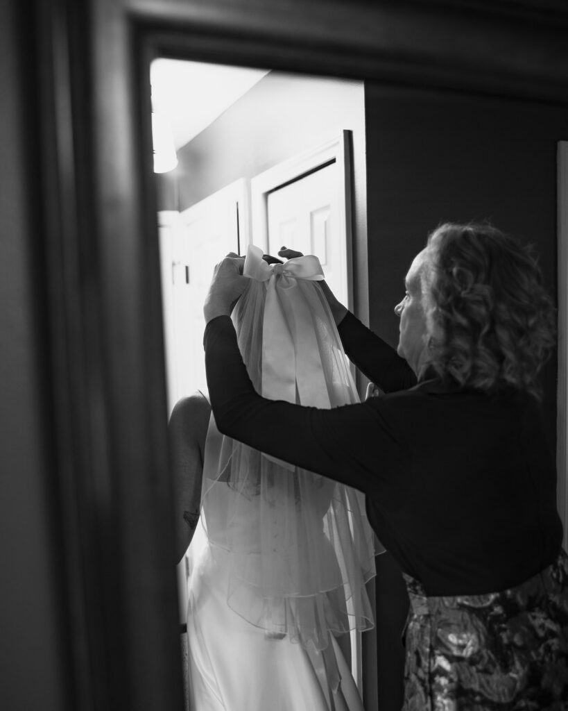 Black and white photo of the brides mother putting in her veil.