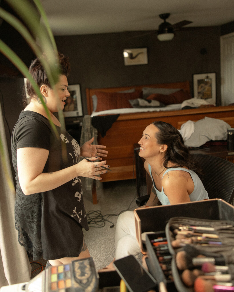 Bride laughing with her makeup artist as she gets ready for her wedding.