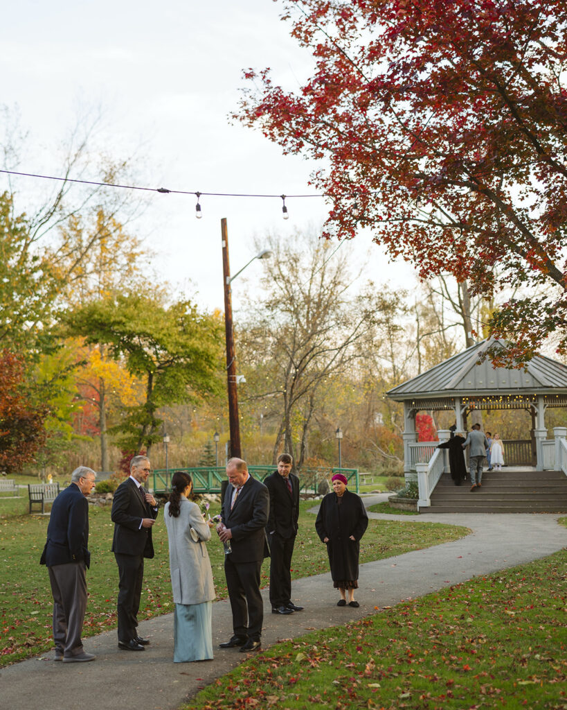 Wedding guests gathering outside near pavilion before ceremony at Depot Park during a Clarkston Michigan wedding.