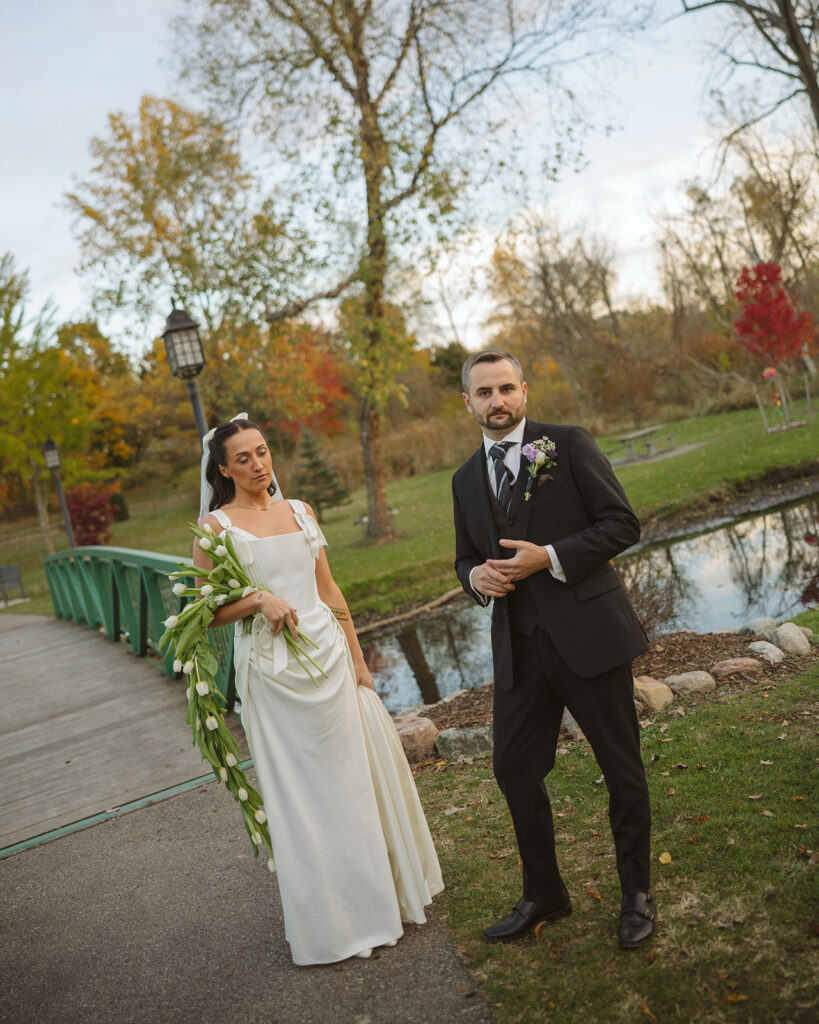 Bride and groom posing together in front of a bridge in fall during portraits at a Clarkston Michigan wedding.