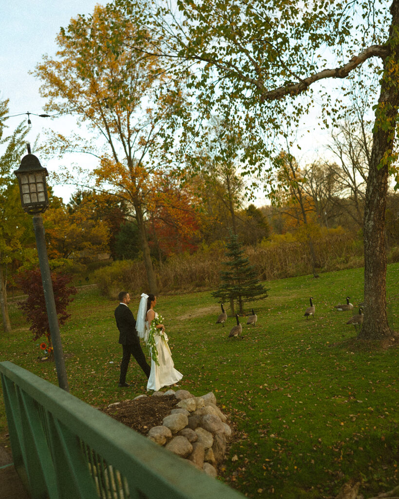 Bride and groom walking through fall foliage near water during portraits at a Clarkston Michigan wedding.