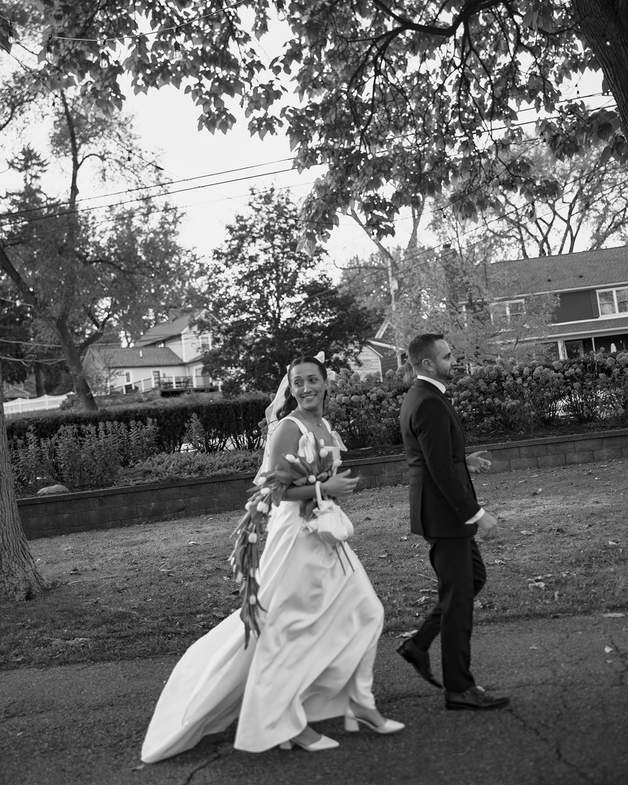 Black and white candid photo of a bride and groom walking to their outdoor ceremony location. 