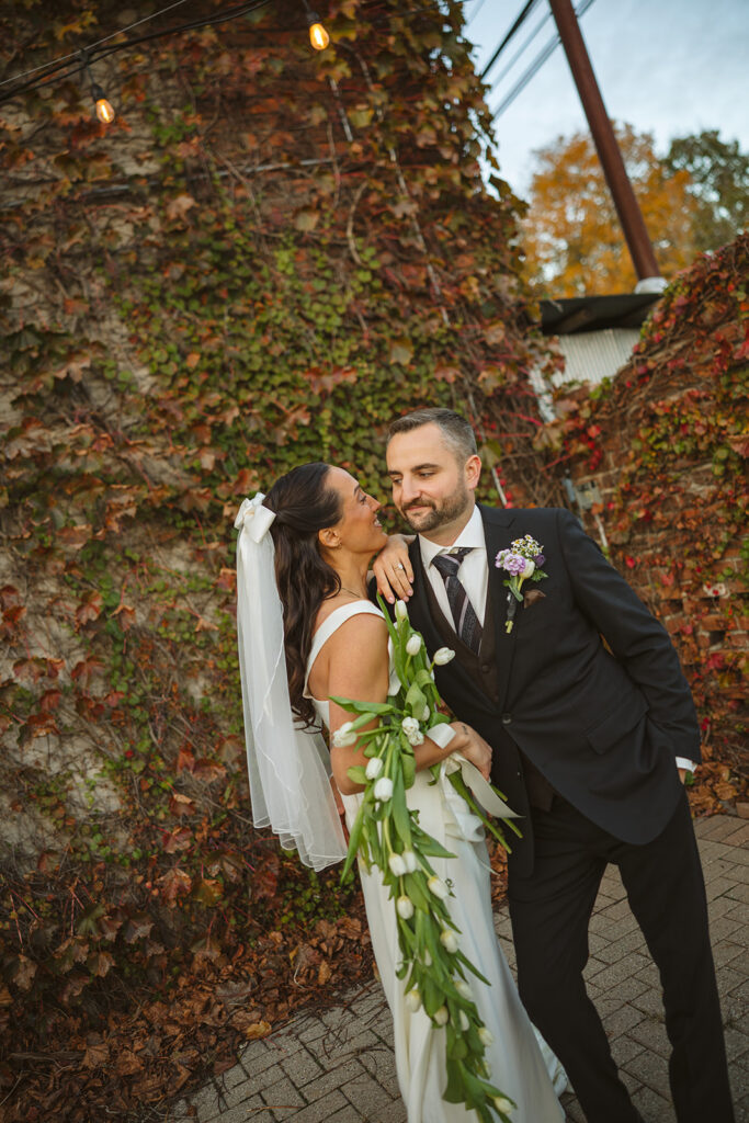 Bride and groom posing together in front of an ivy covered wall in Clarkston, Michigan.