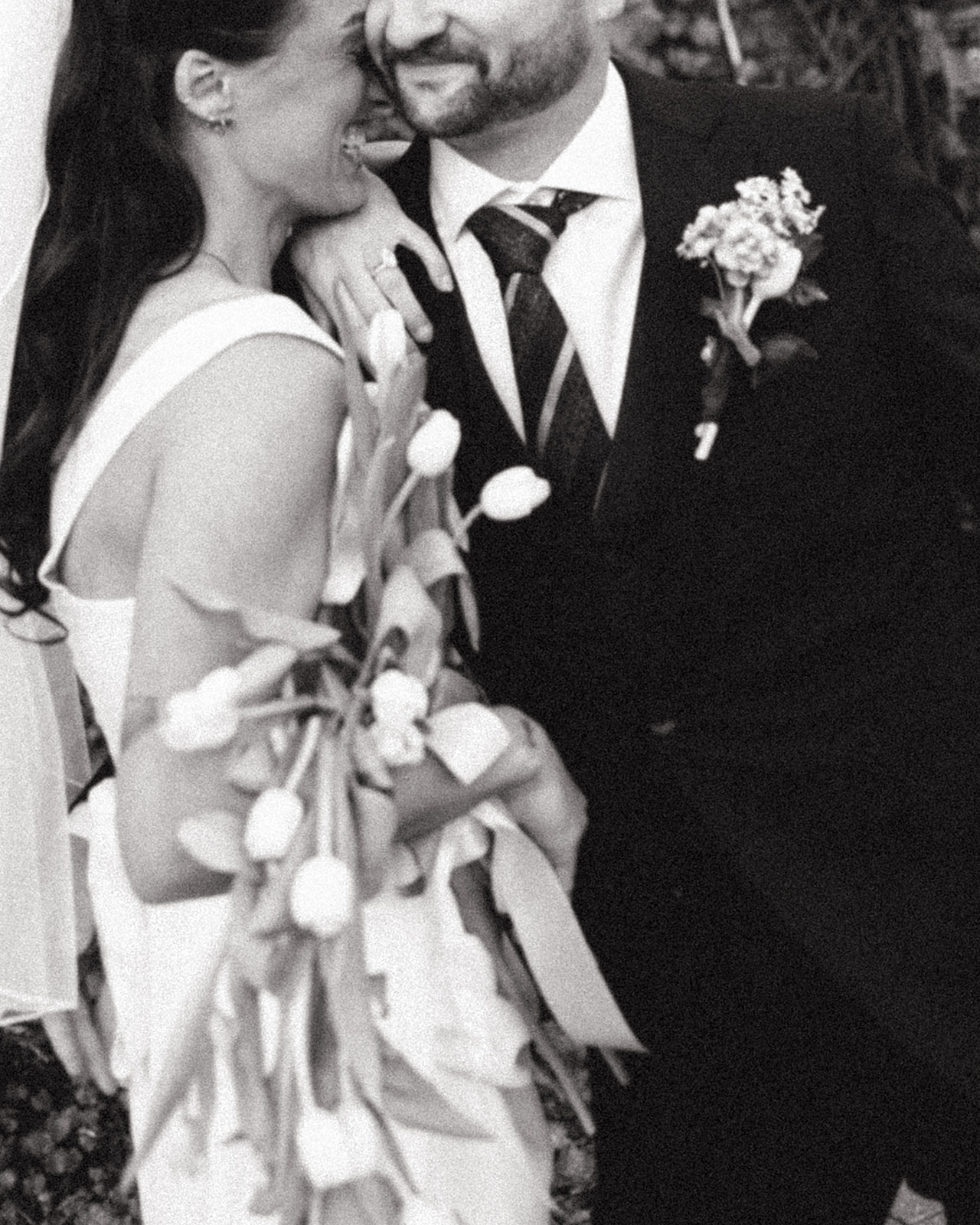 Close up black and white photo of a bride laughing while leaning on the grooms shoulder. 