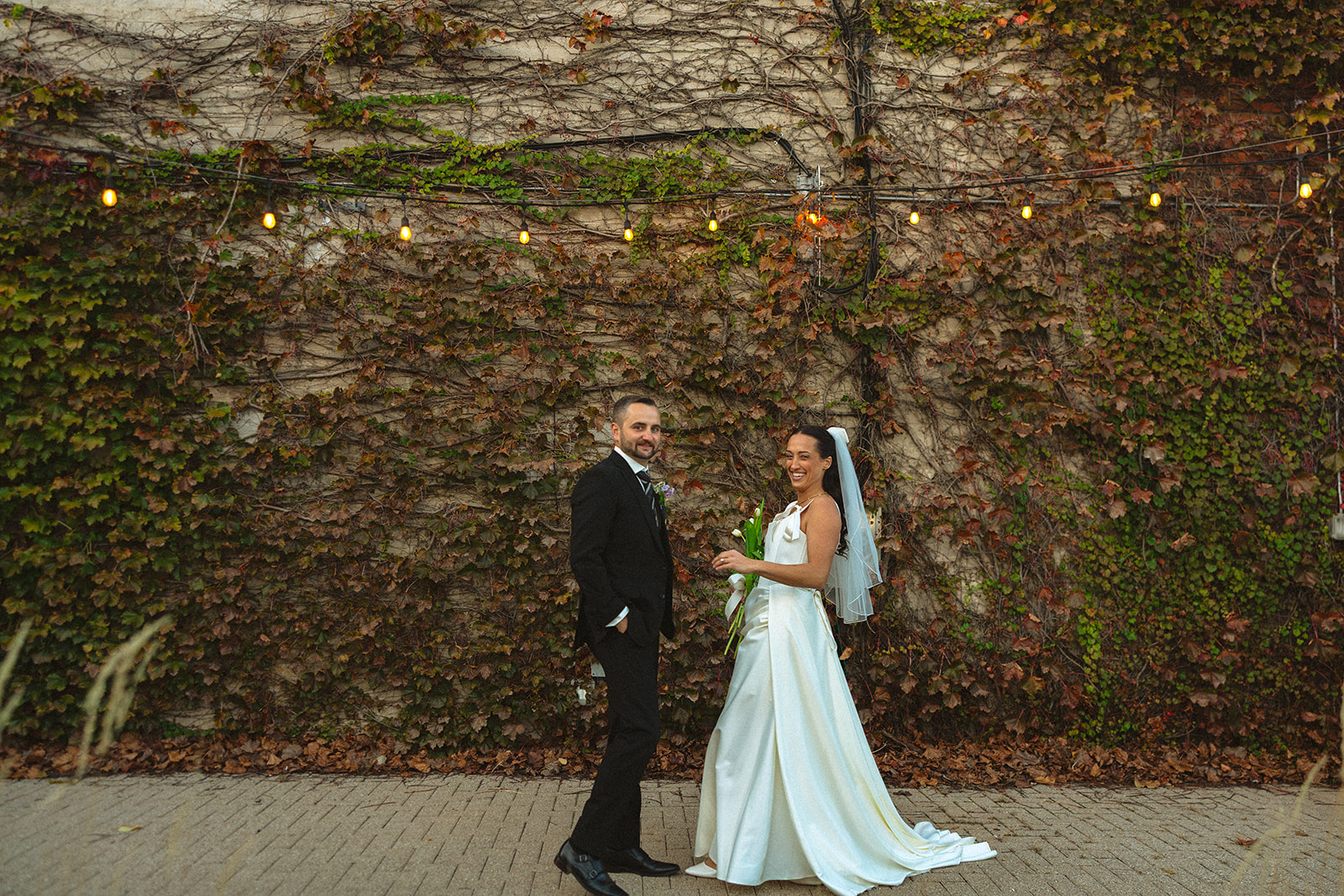 Bride and groom posing for portraits in front of an ivy covered wall. 