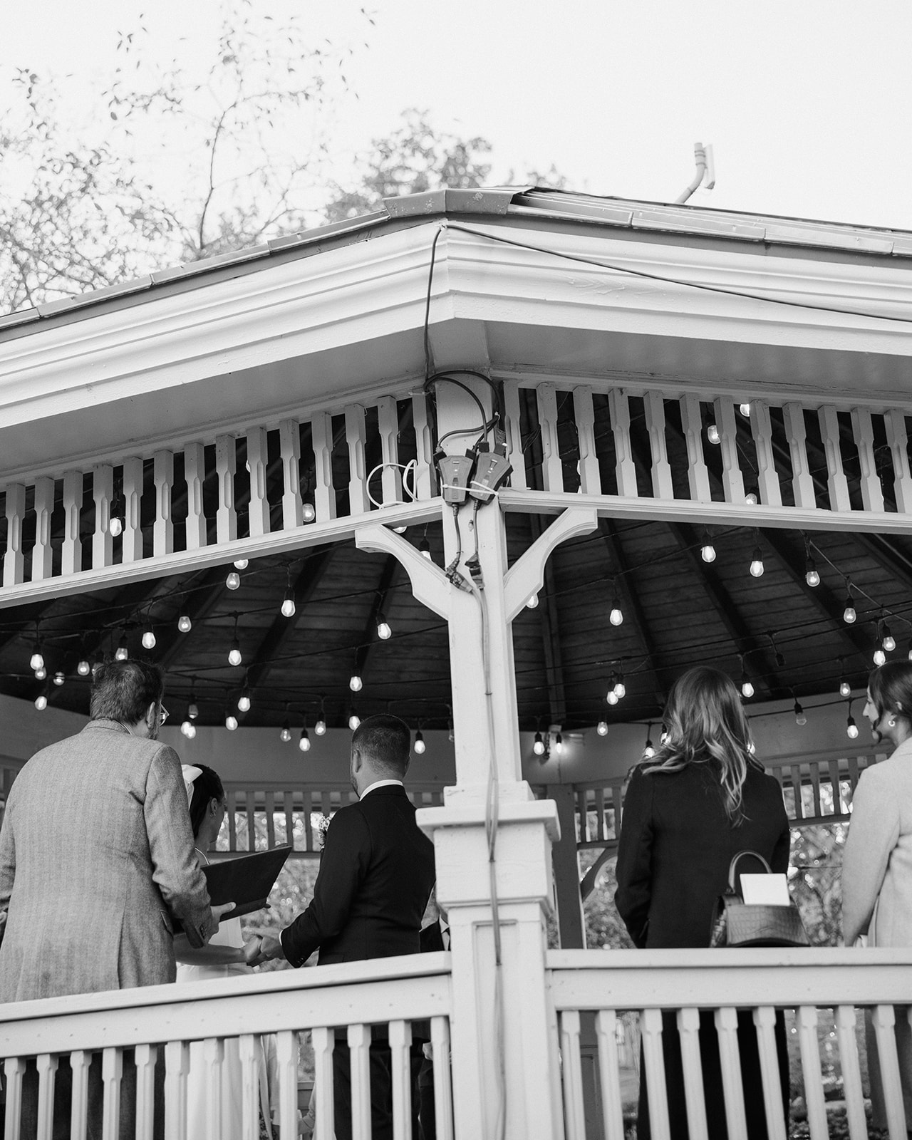 Black and white photo of ceremony under pavilion with string lights at a Clarkston Michigan wedding.