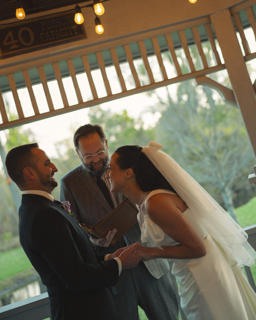 Bride and groom laughing together during vows at Depot Park ceremony in Clarkston Michigan.