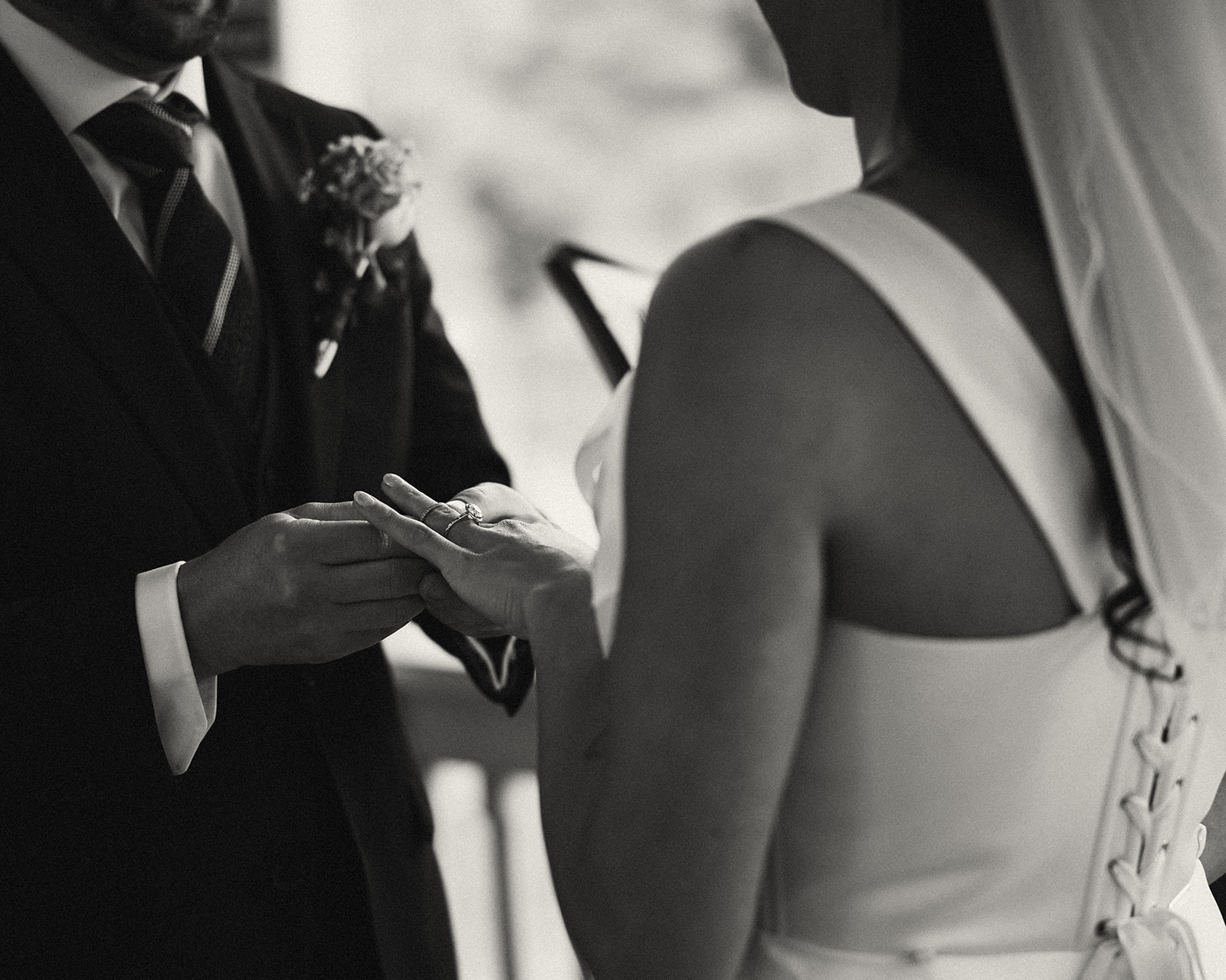 Black and white close up photo of the groom placing the ring on the brides finger. 